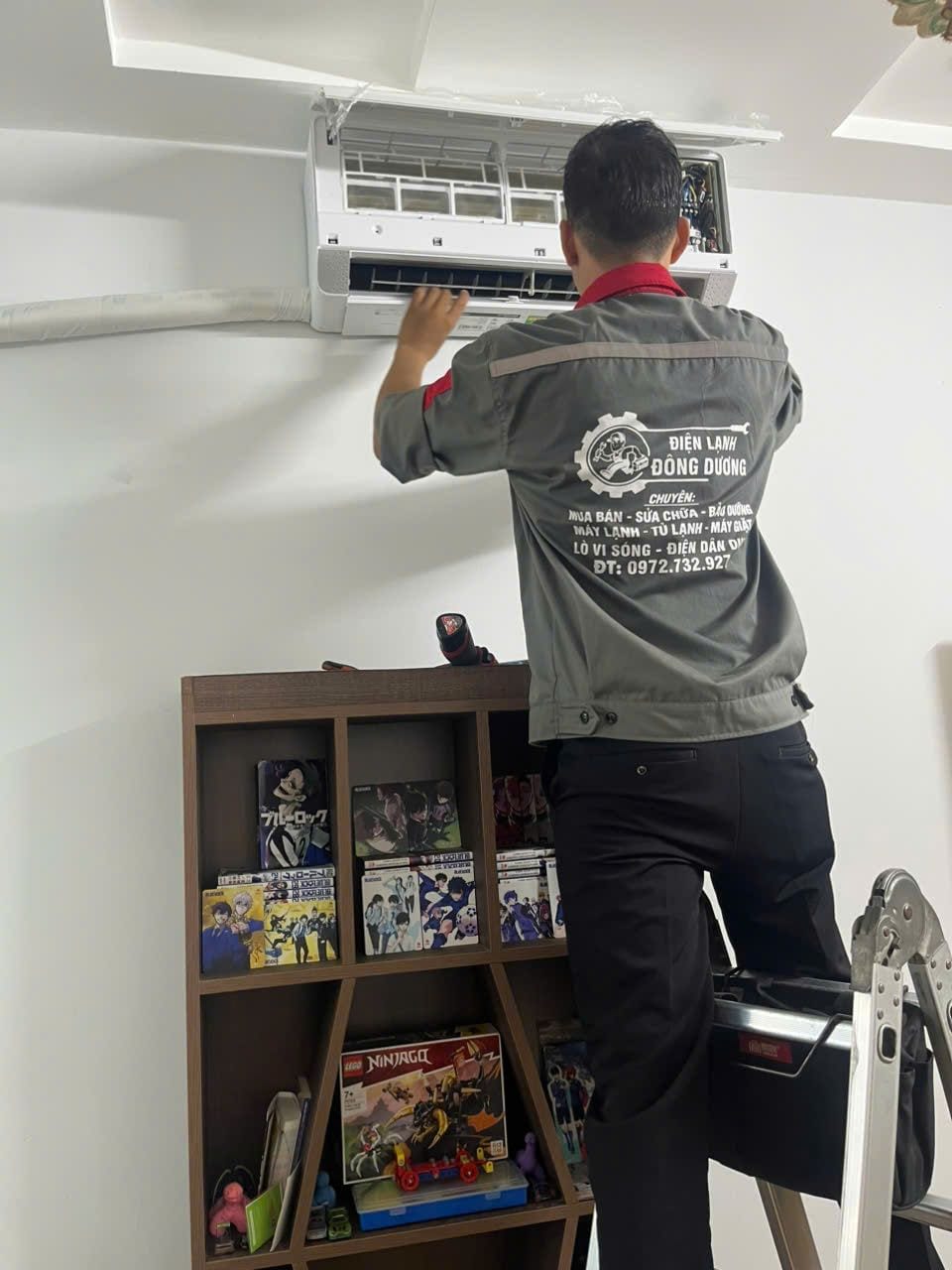 Thợ Điện Lạnh Đông Dương mặc đồng phục đứng trên thang hoàn thiện dàn lạnh máy lạnh trong phòng ngủ